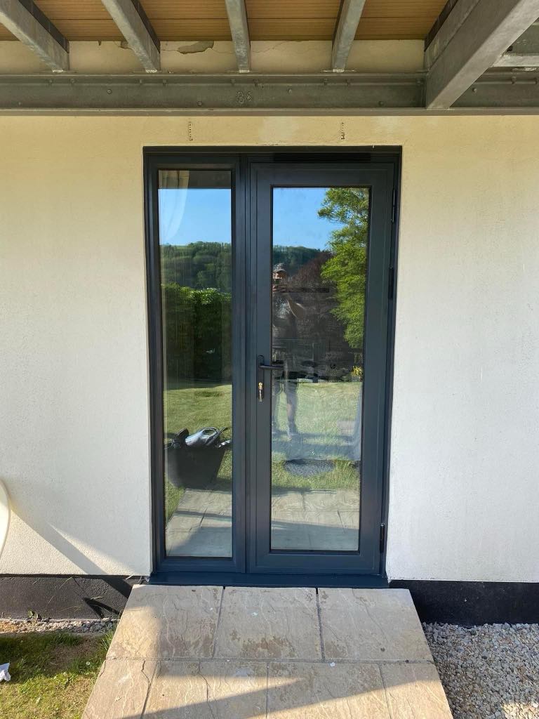 Elegant black French doors installed on the rear of a home, featuring large glass panels and modern handle, opening out to a garden.