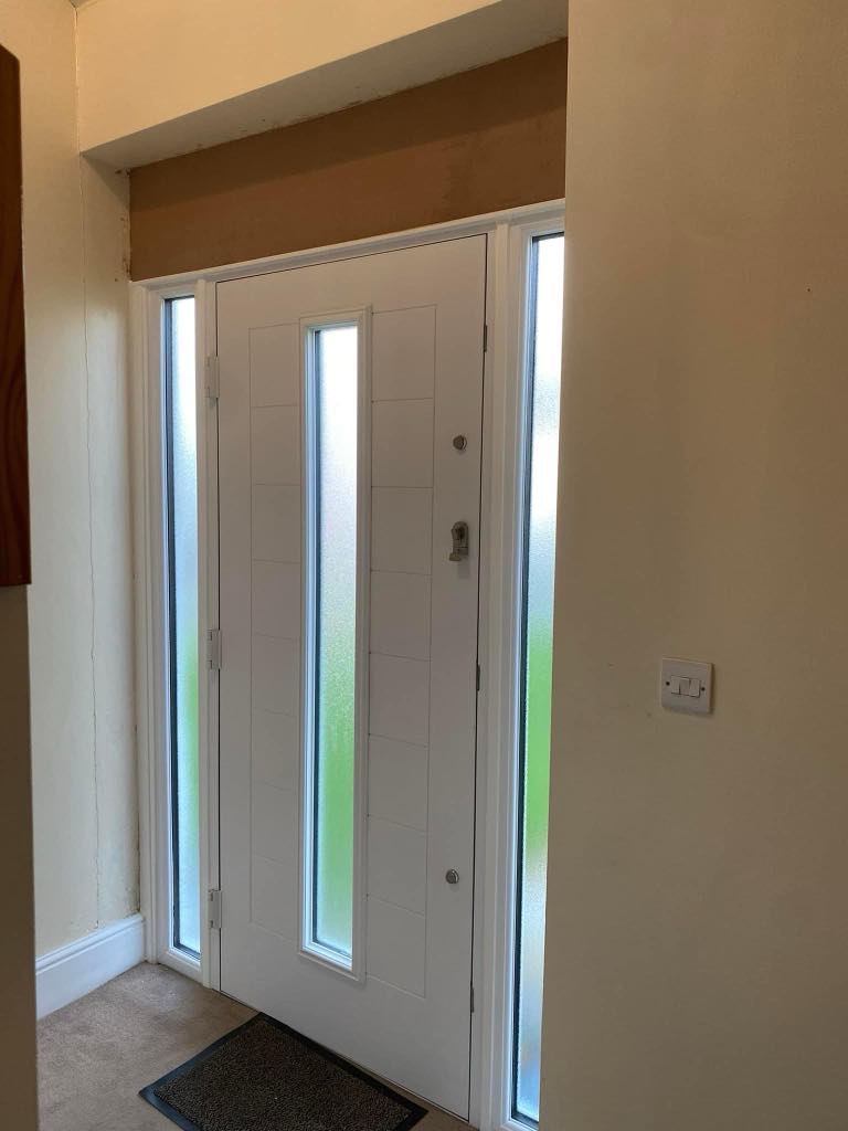 Modern large white front door with glass side panels on both sides, allowing natural light into the entryway of a stylish residential home.